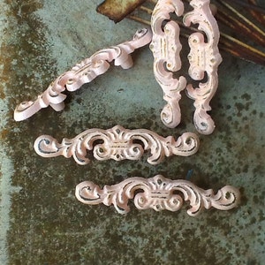 May include: Five antique pink metal drawer pulls with ornate designs. The pulls have a distressed finish and are perfect for adding a vintage touch to furniture.