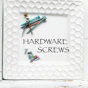 May include: A white ceramic dish with a honeycomb pattern, containing a variety of colorful screws. The dish has the text "HARDWARE SCREWS" written in black.