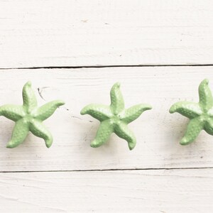 May include: Three light green ceramic starfish on a white wooden surface.