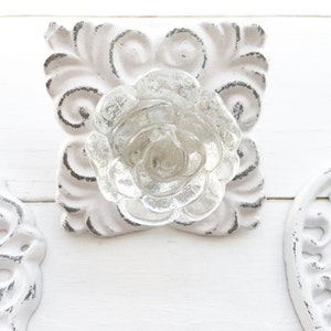 May include: White ceramic drawer pulls with a clear glass rose design. The pulls have a distressed finish and intricate details.