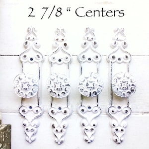 May include: Four white cast iron door knobs with ornate designs. The knobs are 2 7/8 inches apart.