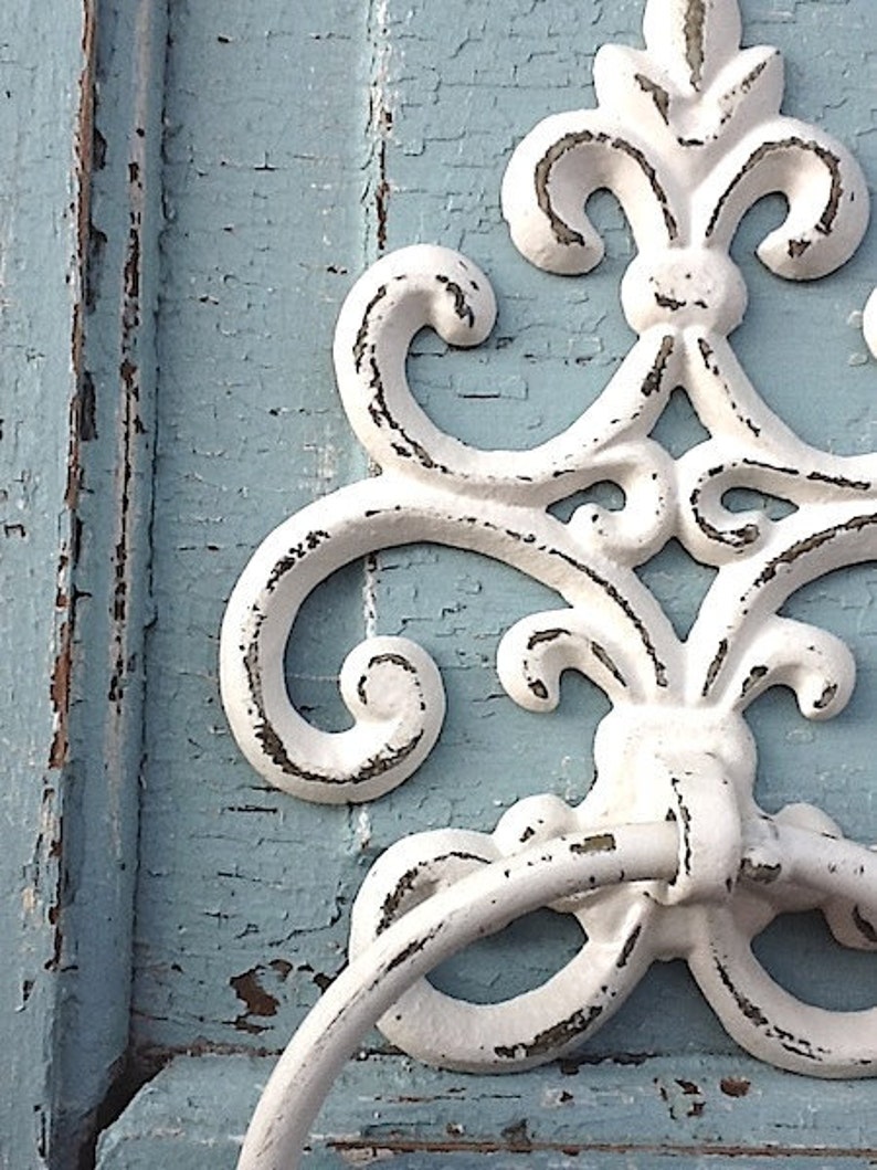 Peut inclure: Crochet d&eacute;coratif en m&eacute;tal blanc avec une poign&eacute;e en anneau fix&eacute;e &agrave; une surface en bois bleu clair. Le crochet a un aspect vieilli et us&eacute;.