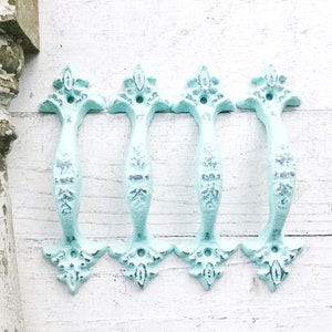 May include: Four antique-style cast iron drawer pulls in a light blue finish. The pulls have a decorative floral design and are perfect for adding a touch of vintage charm to any home.