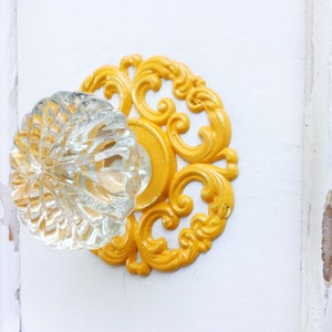 May include: A clear glass door knob with a decorative yellow metal backplate featuring a floral design.