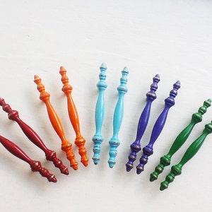 May include: Assortment of colorful wooden drawer pulls with decorative finials. The pulls are in shades of red, orange, blue, green, and purple.