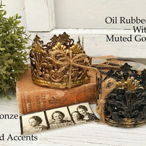 May include: Two decorative metal candle holders with intricate designs. One is antique bronze with muted gold accents, and the other is oil rubbed bronze with muted gold accents.