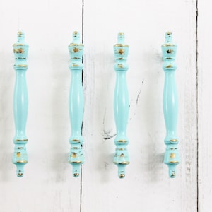 May include: Four light blue cabinet knobs with gold accents. The knobs have a distressed finish and are made of wood.