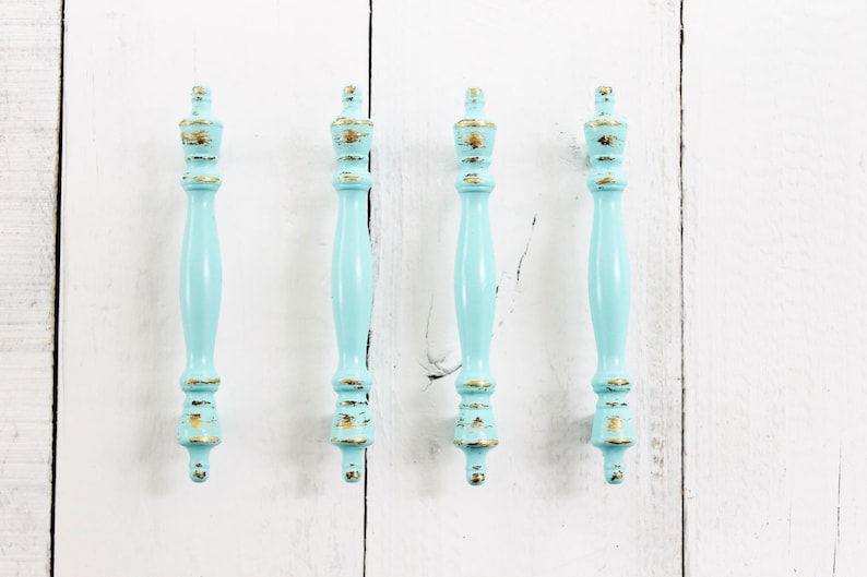 May include: Four light blue cabinet knobs with gold accents. The knobs have a distressed finish and are made of wood.
