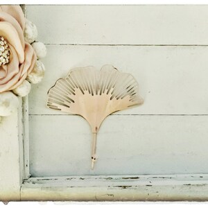 May include: A light pink ginkgo leaf-shaped decorative object on a white wooden background.
