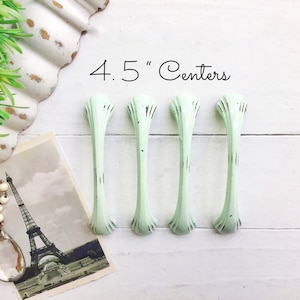 May include: Four light green cabinet pulls with a distressed finish. The pulls are 4.5 inches apart.