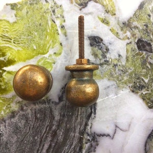 May include: Two antique brass cabinet knobs, one with a threaded stem and the other with a smooth round top. The knobs are displayed on a green and white marble surface.
