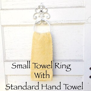 Peut inclure: Un petit anneau de serviette blanc avec un motif d&eacute;coratif enroul&eacute;, tenant une serviette de toilette jaune. Le texte "Small Towel Ring With Standard Hand Towel" est sous la serviette.