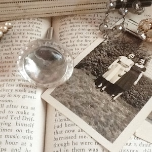 May include: A vintage book with a magnifying glass on top of it. The book has text about a family gathering and a photo of three people standing in a field. The photo is in black and white.