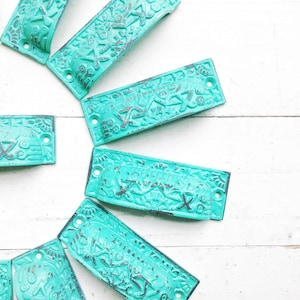 May include: A collection of turquoise blue drawer pulls with an ornate design. The pulls are arranged in a circle on a white surface.