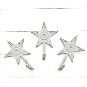 May include: Three white metal star-shaped hooks mounted on a white wooden wall.
