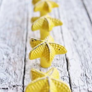 May include: Five yellow ceramic starfish drawer pulls in a row on a white wooden surface.
