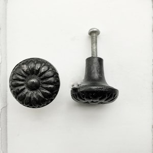 May include: Two black cabinet knobs with a floral design. One knob is a round knob with a raised floral design. The other knob is a round knob with a raised floral design and a short stem.