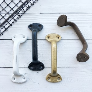 May include: Four cabinet pulls in different finishes: white, black, gold, and brown. The pulls are all the same style, with a rounded top and two holes for mounting.