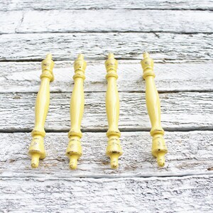 May include: Five yellow wooden finials with a distressed finish. The finials are arranged in a row on a white wooden surface.