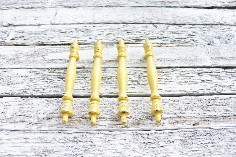 May include: Five yellow wooden finials with a distressed finish. The finials are arranged in a row on a white wooden surface.