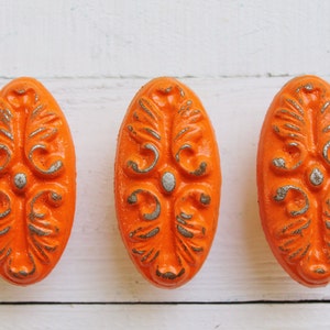 May include: Three oval-shaped orange drawer pulls with a silver floral design.
