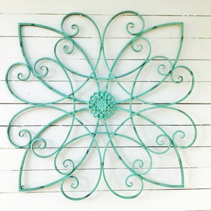May include: A teal metal wall decor in the shape of a flower with intricate swirls and a smaller circular design in the center.