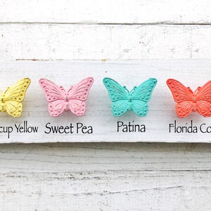 May include: Four butterfly-shaped hooks in different colors: Butterscotch Yellow, Sweet Pea, Patina, and Florida Coral.