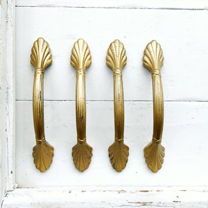 May include: Four gold-toned cabinet pulls with a shell-like design. The pulls have a slightly curved shape and a smooth finish.