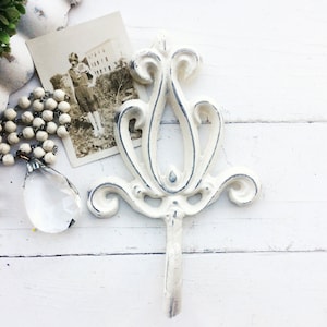 May include: White metal decorative hook with a floral design. The hook is distressed and has a vintage look.