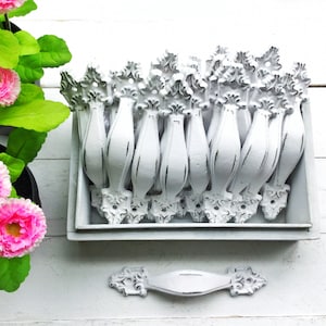 May include: A box of white, ornate drawer pulls with a distressed finish. The pulls are arranged in rows and are ready to be used for furniture or home decor projects.