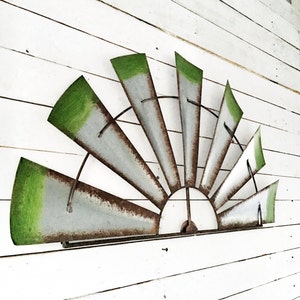 May include: A large metal windmill wall decor with green and silver painted blades. The blades are arranged in a semi-circle shape and are attached to a metal frame.