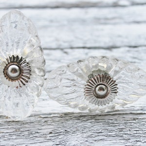 May include: Two clear glass cabinet knobs with a scalloped design and silver metal accents.