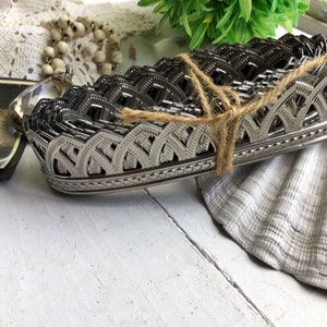 May include: A silver metal trim with a decorative scalloped design. The trim is tied together with twine and is stacked on top of itself.
