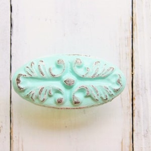 May include: A light blue oval-shaped cabinet knob with a decorative, distressed, floral design.