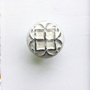 May include: White cabinet knob with a decorative, raised, black and white design.