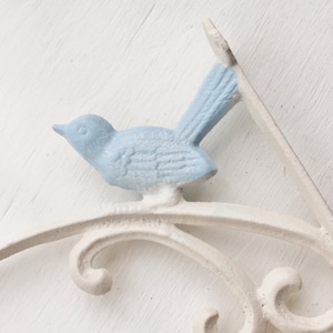 May include: White metal shelf bracket with a blue bird design. The bracket has a decorative scrollwork design.