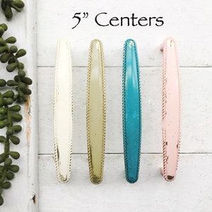 May include: Four 5" center cabinet pulls in white, beige, teal, and pink. Each pull has a rope-like design around the edge.