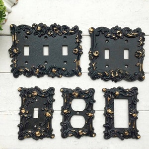 May include: Set of five black and gold decorative light switch and outlet covers with ornate floral designs.