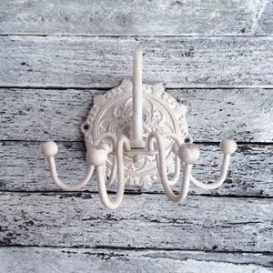 Puede incluir: Perchero de metal blanco con un dise&ntilde;o floral decorativo. El perchero tiene cinco ganchos y est&aacute; montado en una pared.