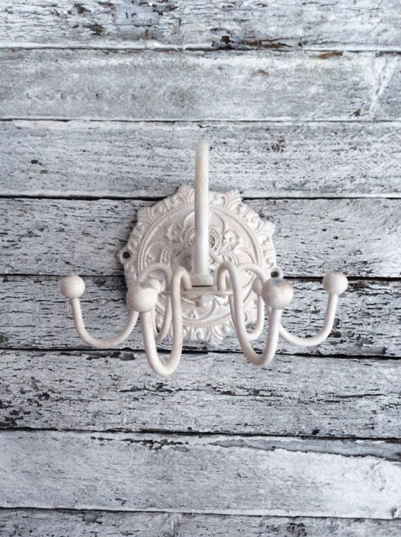 Puede incluir: Perchero de metal blanco con un dise&ntilde;o floral decorativo. El perchero tiene cinco ganchos y est&aacute; montado en una pared.