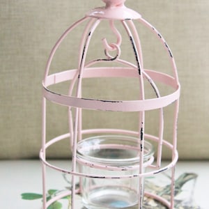 May include: Pink metal birdcage candle holder with a small glass votive inside. The birdcage has a distressed finish and a pink bird on top.