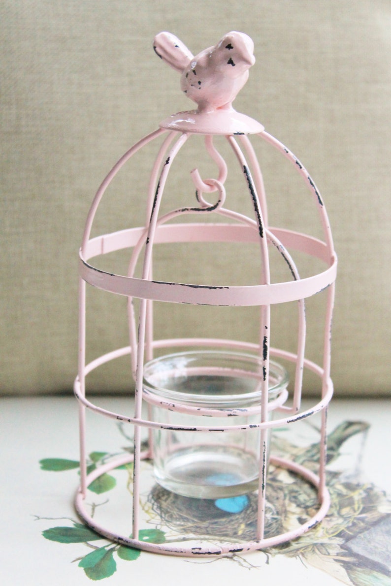 May include: Pink metal birdcage candle holder with a small glass votive inside. The birdcage has a distressed finish and a pink bird on top.