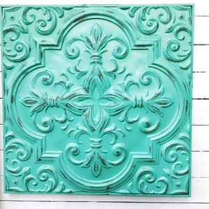 May include: A teal blue metal wall decor tile with an ornate, embossed design. The tile has a distressed finish, giving it a vintage look.