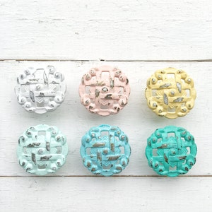 May include: Six decorative cabinet knobs in various pastel colors, including white, pink, yellow, blue, and turquoise. Each knob features a silver-toned, geometric design.