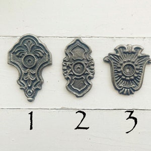 May include: Three ornate metal decorative accents with a circular center hole. The accents are numbered 1, 2, and 3.