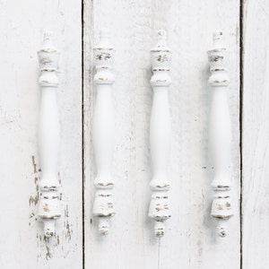 May include: Four white wooden drawer pulls with a distressed finish. The pulls have a decorative top and a long, slender body.