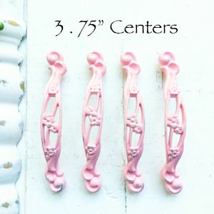 May include: Four pink metal drawer pulls with a floral design. The pulls are 3.75 inches apart.