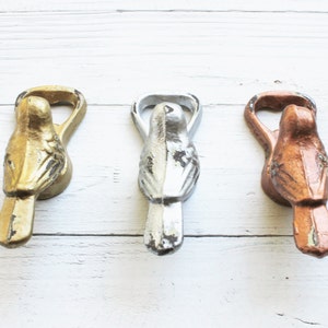 May include: Three bird-shaped bottle openers in gold, silver, and copper finishes. Each opener has a bird design with a wingspan and a small opening for the bottle cap.