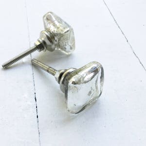 May include: Two silver square glass cabinet knobs with a clear glass finish. The knobs have a silver metal base and screw.