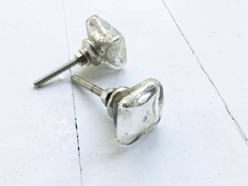 May include: Two silver square glass cabinet knobs with a clear glass finish. The knobs have a silver metal base and screw.
